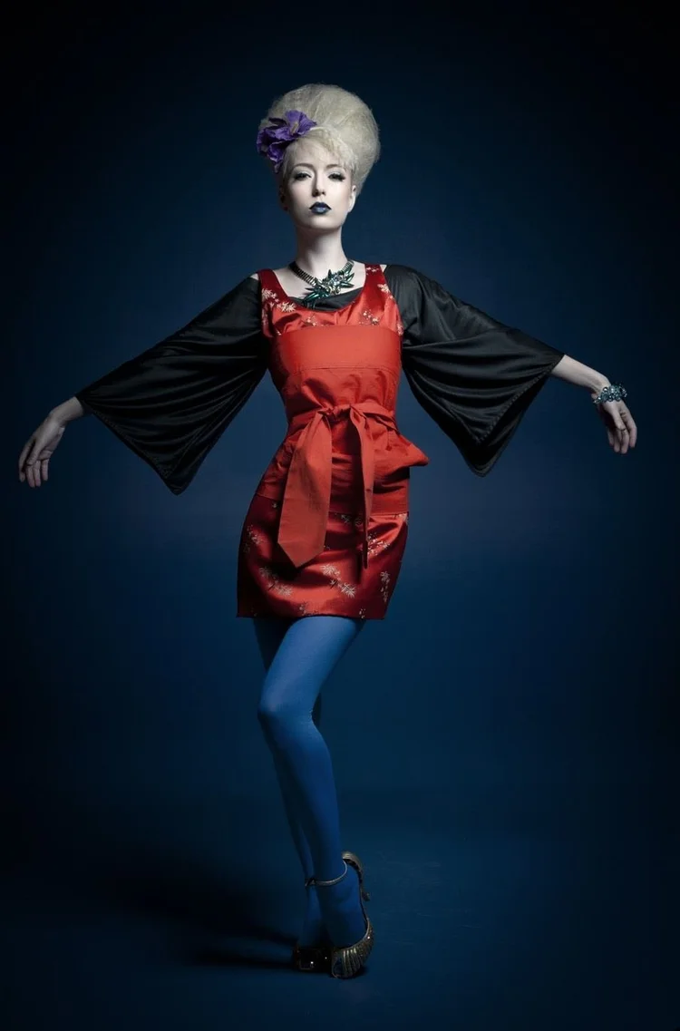 Full length in a red dress with black kimono sleeves and blue tights on a navy ground
