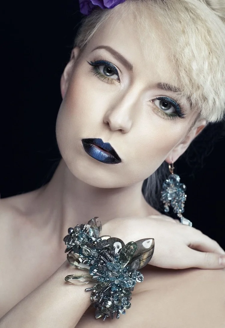 Close portrait: platinum hair, blue lips, an Andrea Li blue crystal cluster earring and a matching cuff on the arm resting across her shoulder