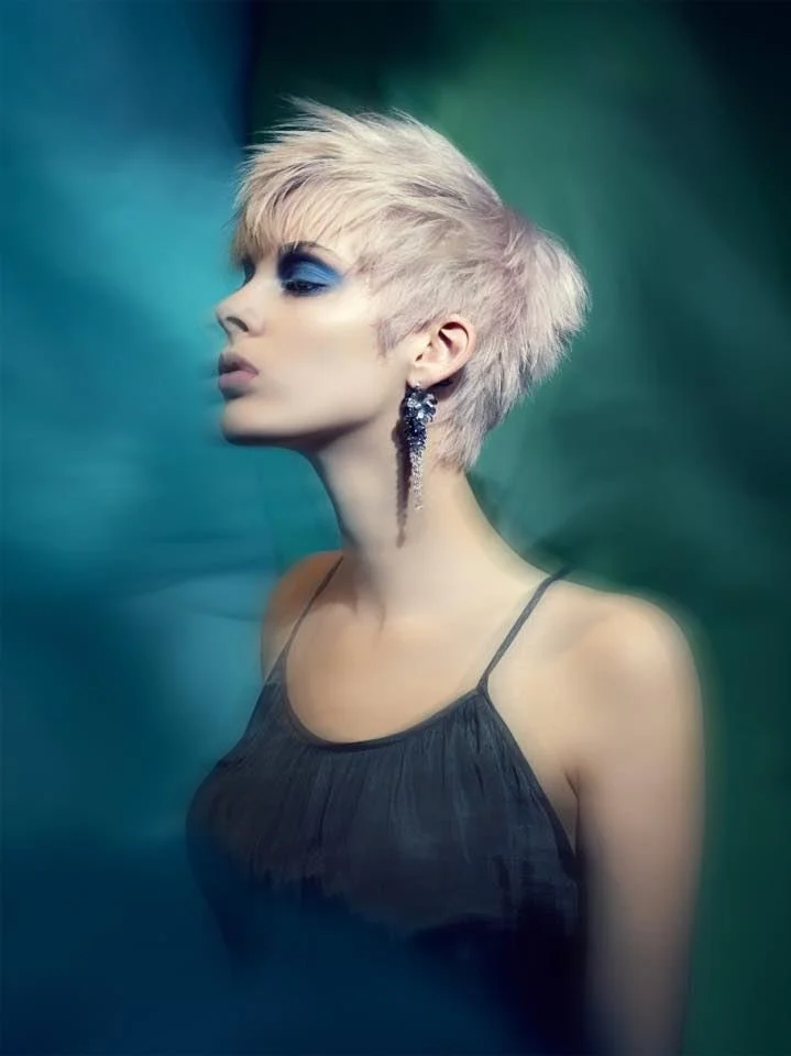 Short pink pixie hair in profile with a long cascading Andrea Li cluster earring on a teal ground