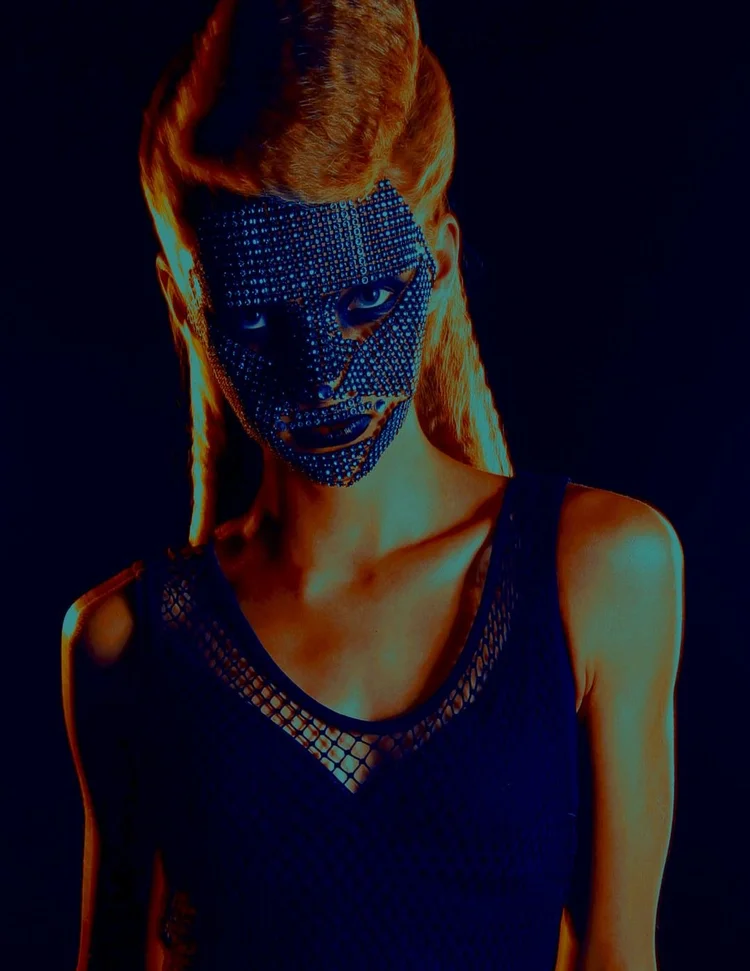 A crystal face mask and a fishnet top under red light