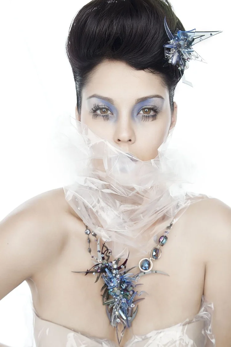 A dark-haired model wrapped in clear plastic with an Andrea Li blue spiky cluster necklace and hair piece
