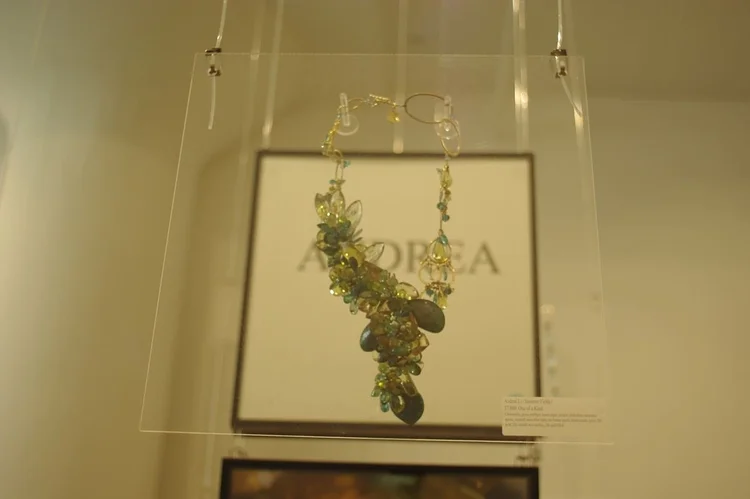 An Andrea Li green and blue gemstone cluster necklace hanging in front of her placard