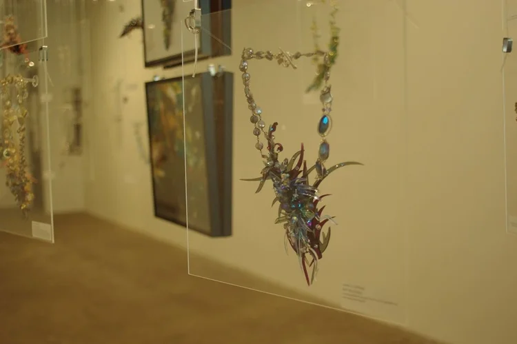 An Andrea Li blue spiked cluster necklace on a clear panel beside a framed print