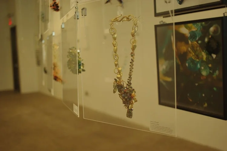 An Andrea Li gold chain necklace with a gemstone cluster, in front of a framed print of her work