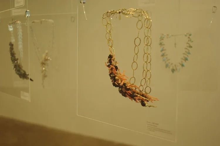 An Andrea Li orange cluster on a long gold chain, on a clear hanging panel