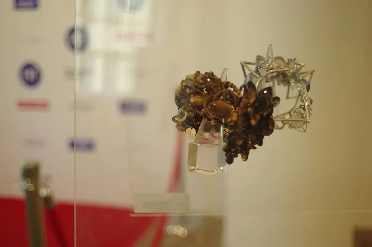 An Andrea Li smoky gemstone cluster piece on a clear stand, the sponsor wall behind