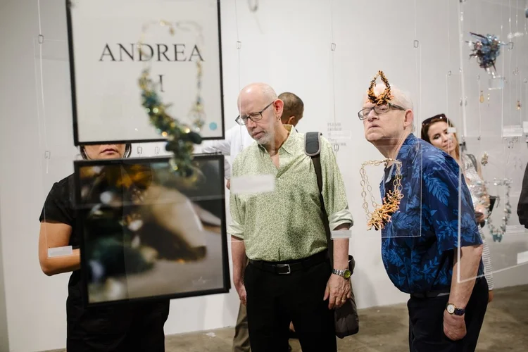 Two men closely examining an Andrea Li orange cluster necklace beneath her placard