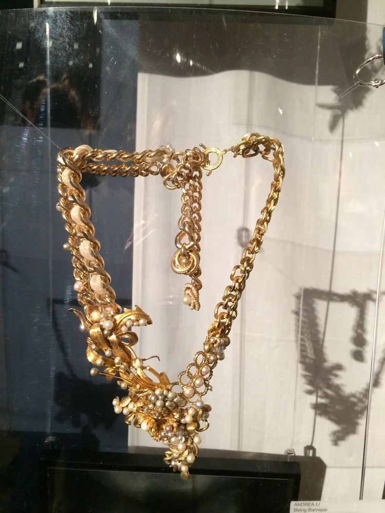 An Andrea Li gold chain necklace with gold leaf and pearl cluster hanging over a shadow box