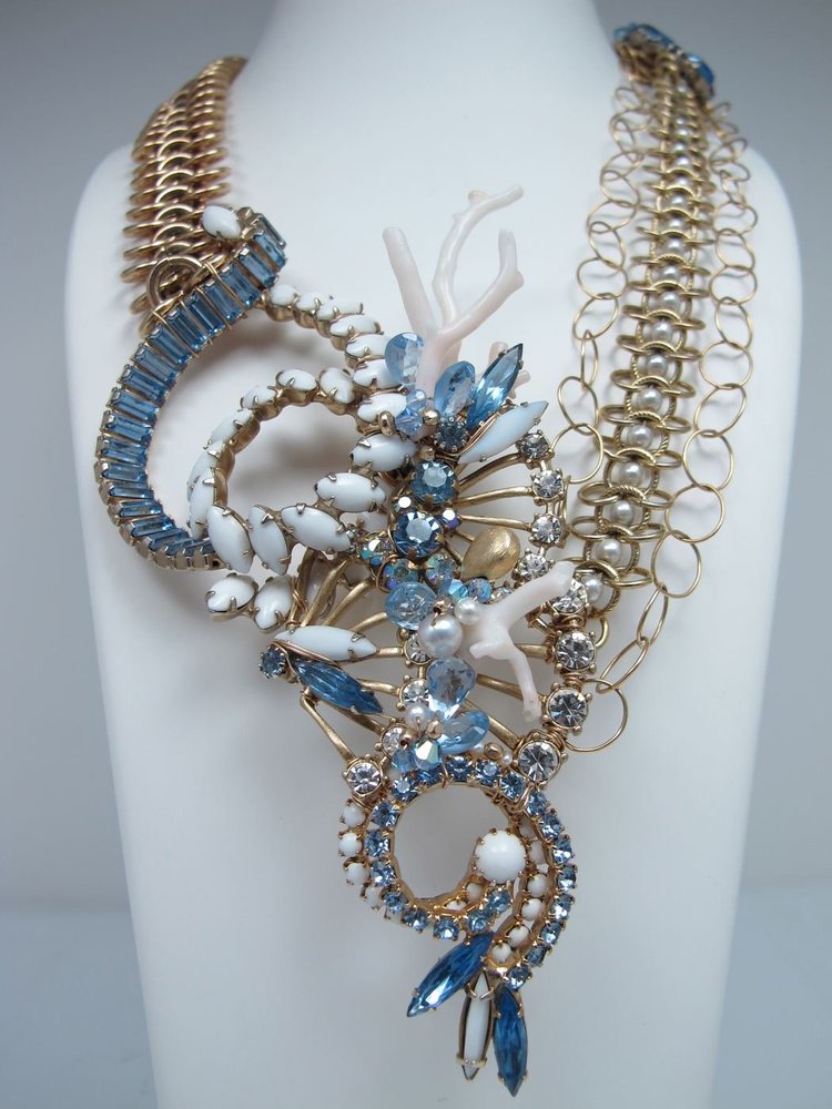 Studio photo on a white bust: an Andrea Li gold chain necklace with blue rhinestone and white coral-like cluster