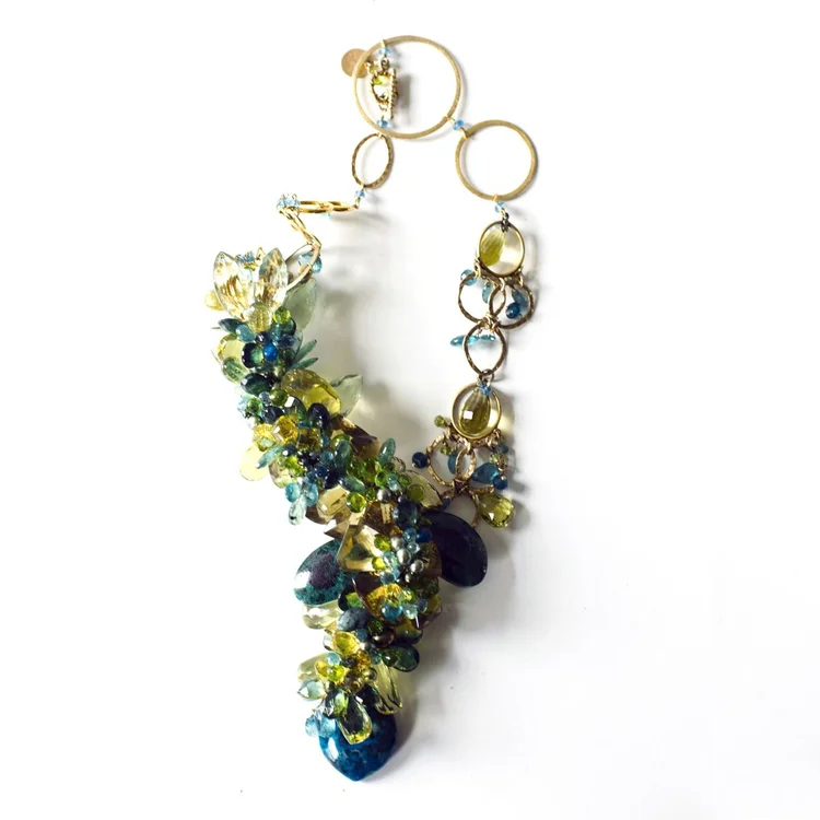 Product photo on white: an asymmetric gold ring-link necklace with blue, green and yellow gemstone clusters