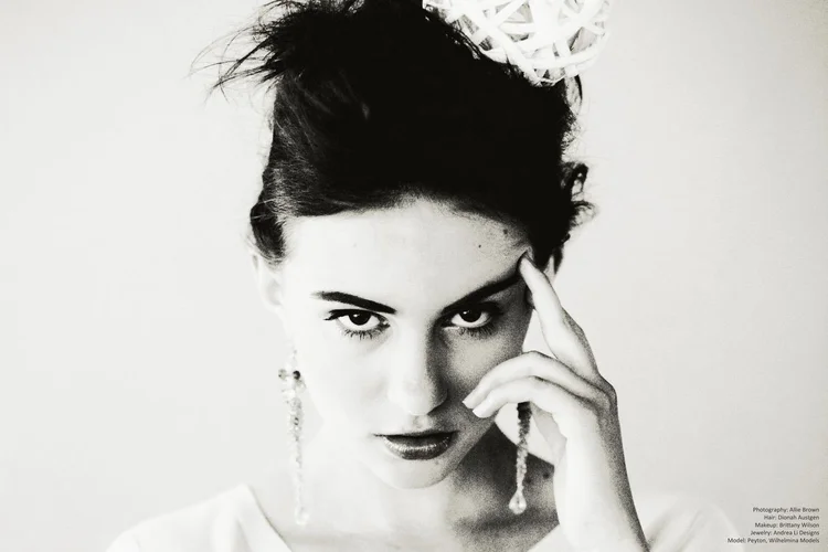 Black and white portrait: a hand at the temple, a long Andrea Li drop earring and a floral headpiece