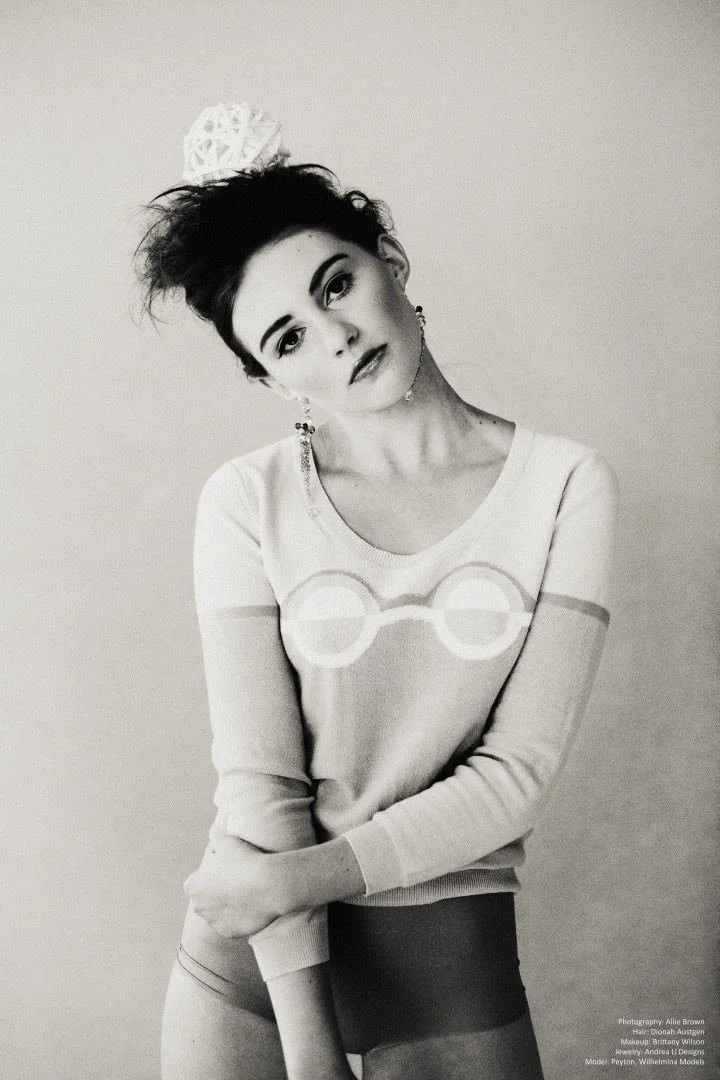 Black and white: the model in the glasses-motif sweater, seated, hair ornament
