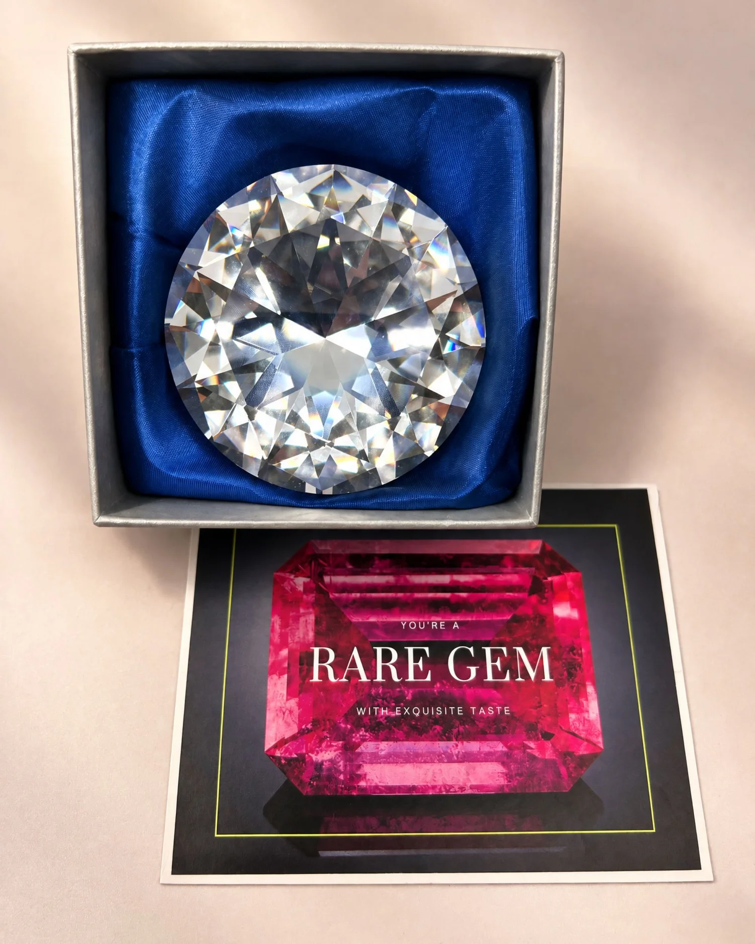 A crystal gem paperweight in a silver gift box lined with blue satin, beside a card that reads You're a Rare Gem, with exquisite taste