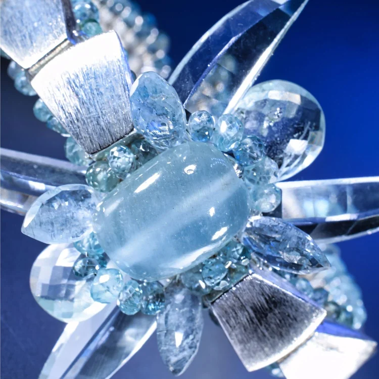 Macro of an Andrea Li statement cuff: a milky aquamarine cabochon framed by brushed silver petals on deep blue, by Andrea Li