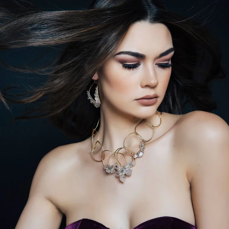 A model with long dark hair in a strapless top wearing a gold link statement necklace with clear stones