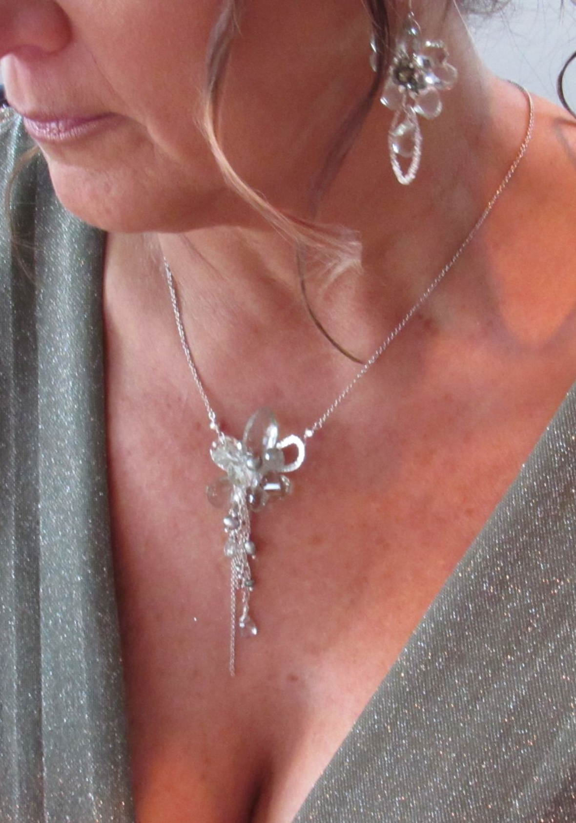 Close-up of a mother of the groom wearing a shimmering silver gown with a matching silver floral pendant necklace and dangling statement earring set.