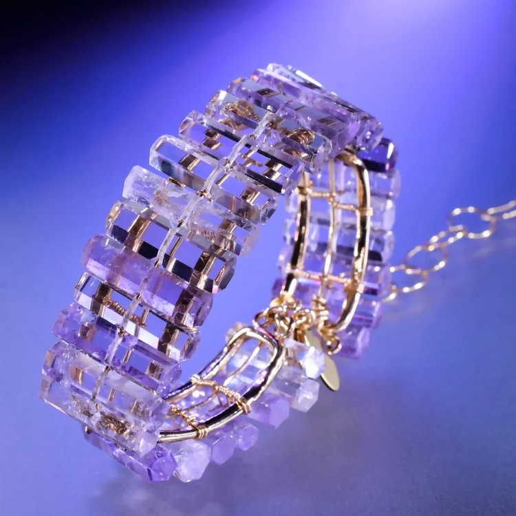 The Purple Amethyst Cuff: rows of pale purple amethyst crystals wired along gold bars, on a blue backdrop