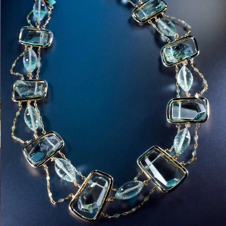 The Green Amethyst Collar: pale green faceted stones in gold frames joined by fine chain, on a blue backdrop