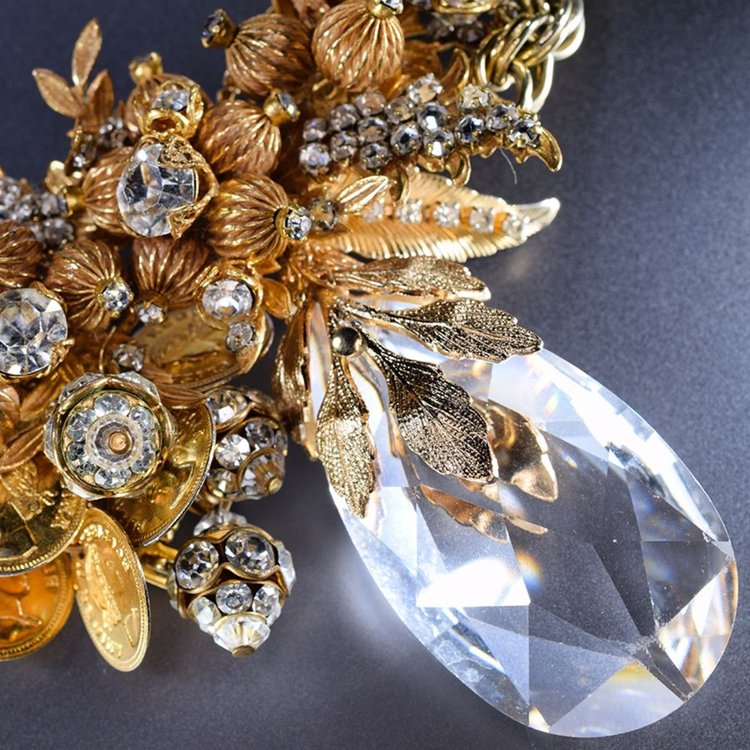 Close-up of vintage gold leaf and crystal components above a large faceted clear crystal drop
