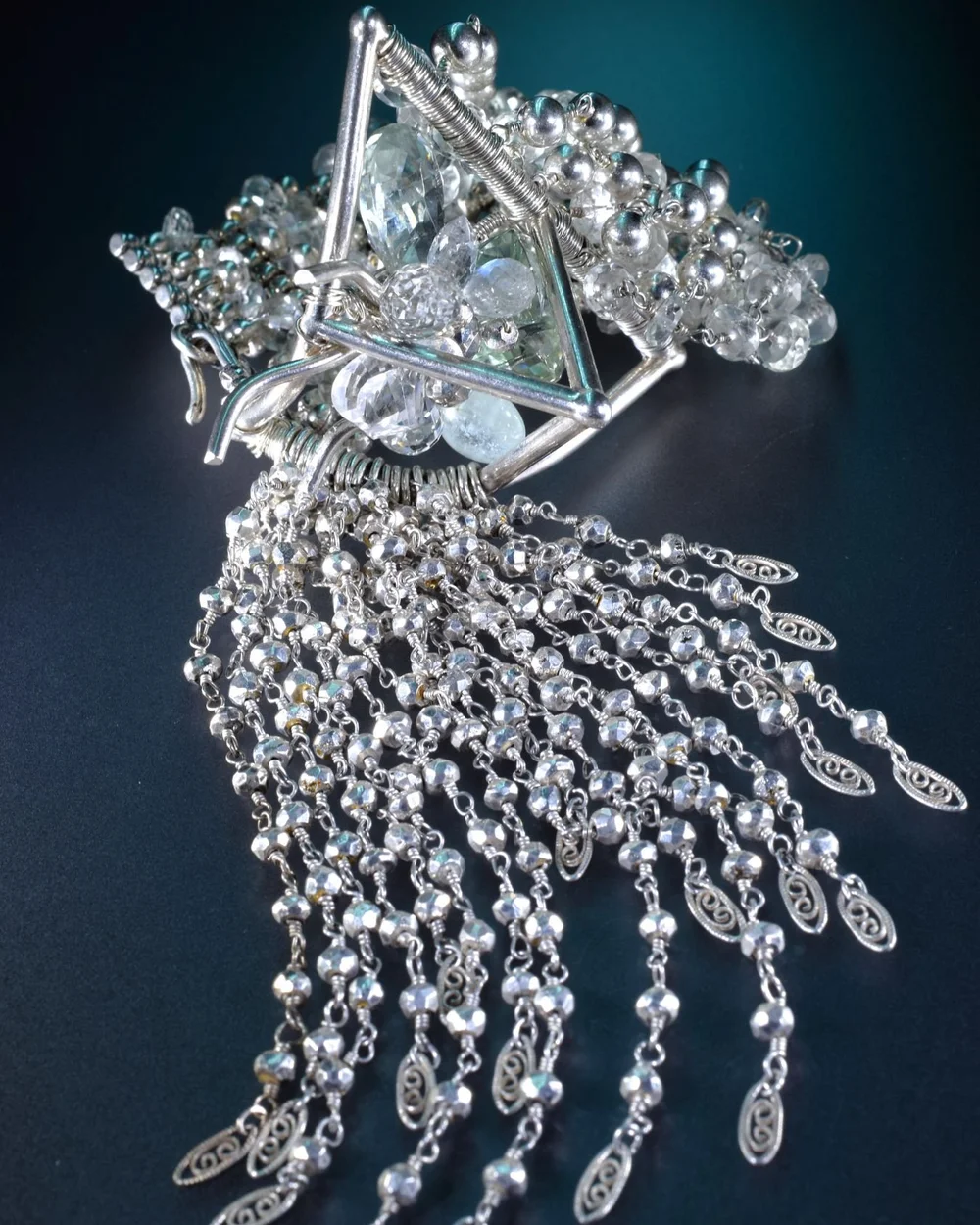 Macro of an Andrea Li silver statement cuff with a triangle-set gemstone and a cascade of silver chains, by Andrea Li