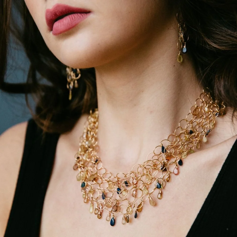 Close-up of an Andrea Li gold chain-link statement collar with dark blue gemstone drops, worn with a black top