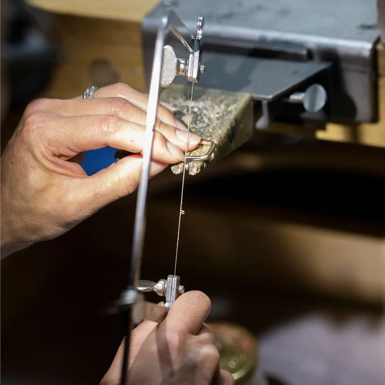 A jeweler's saw cutting through metal held against the bench pin