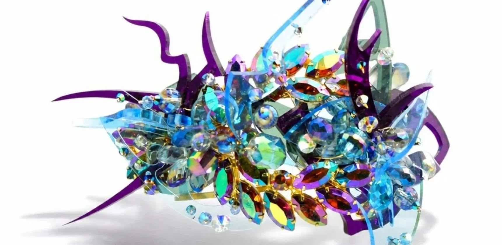 A sculptural piece of iridescent faceted crystals in gold settings, sprung with translucent purple and blue cut shapes, on white