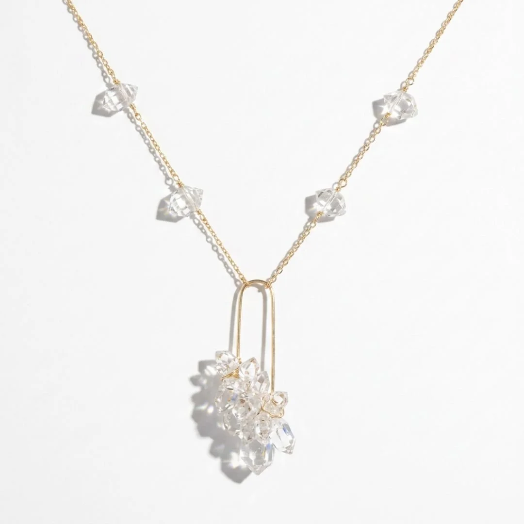 Delicate gold necklace with clear crystal accents and an open-frame pendant cluster, photographed on a soft white background.