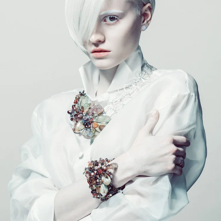 A platinum-haired model in a white shirt wearing an Andrea Li multicolor gemstone statement cuff and brooch, by Andrea Li