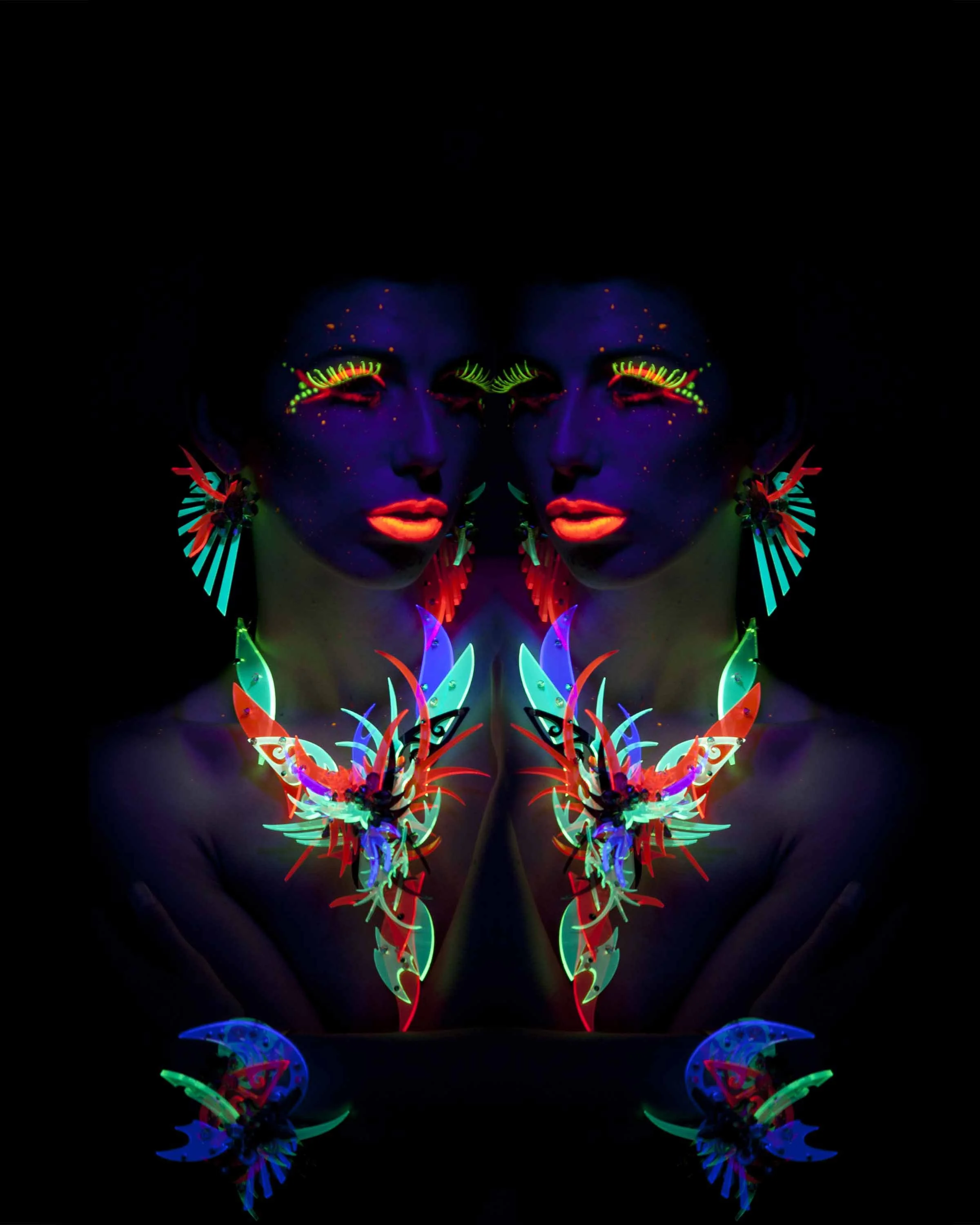 Mirrored blacklight portrait of a model in neon makeup wearing fluorescent statement jewelry against a deep black background.