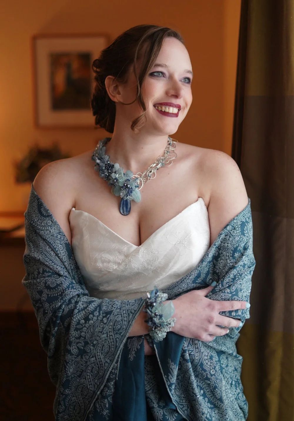Victoria smiling in a strapless ivory gown and a blue paisley shawl, wearing a silver wire necklace with a cluster of blue gemstones and a matching blue gemstone cuff