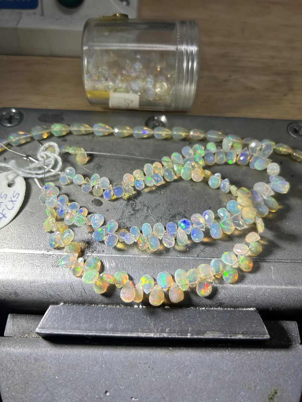 Strands of opal briolettes flashing color on Andrea Li's bench block, a jar of opals behind them