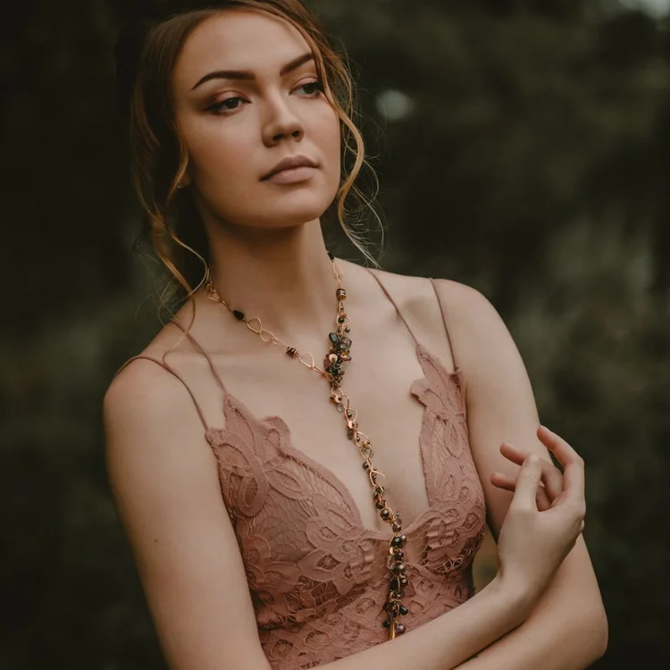 A model in a blush lace slip dress wearing a long gemstone pendant necklace