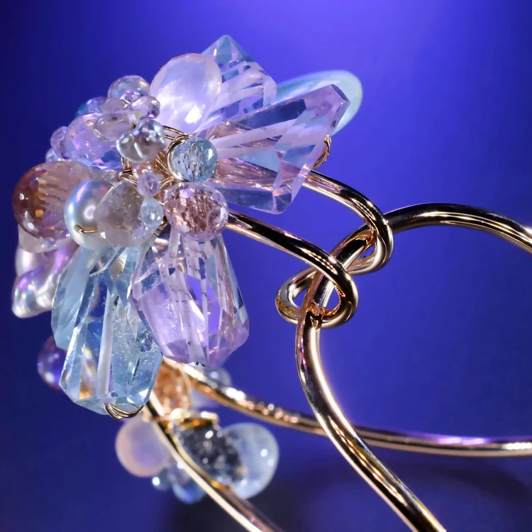 The Pastel Gemstone Statement Cuff: a cluster of lilac, aqua and clear crystals on looping gold wire, on a blue backdrop