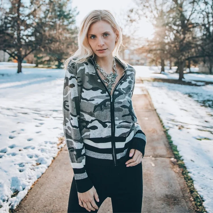 Model in a camouflage jacket on a snowy path, wearing a vintage statement necklace