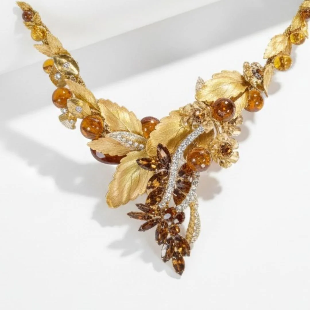 Close-up of an ornate gold leaf necklace with amber gemstones and sparkling floral details on a white background.