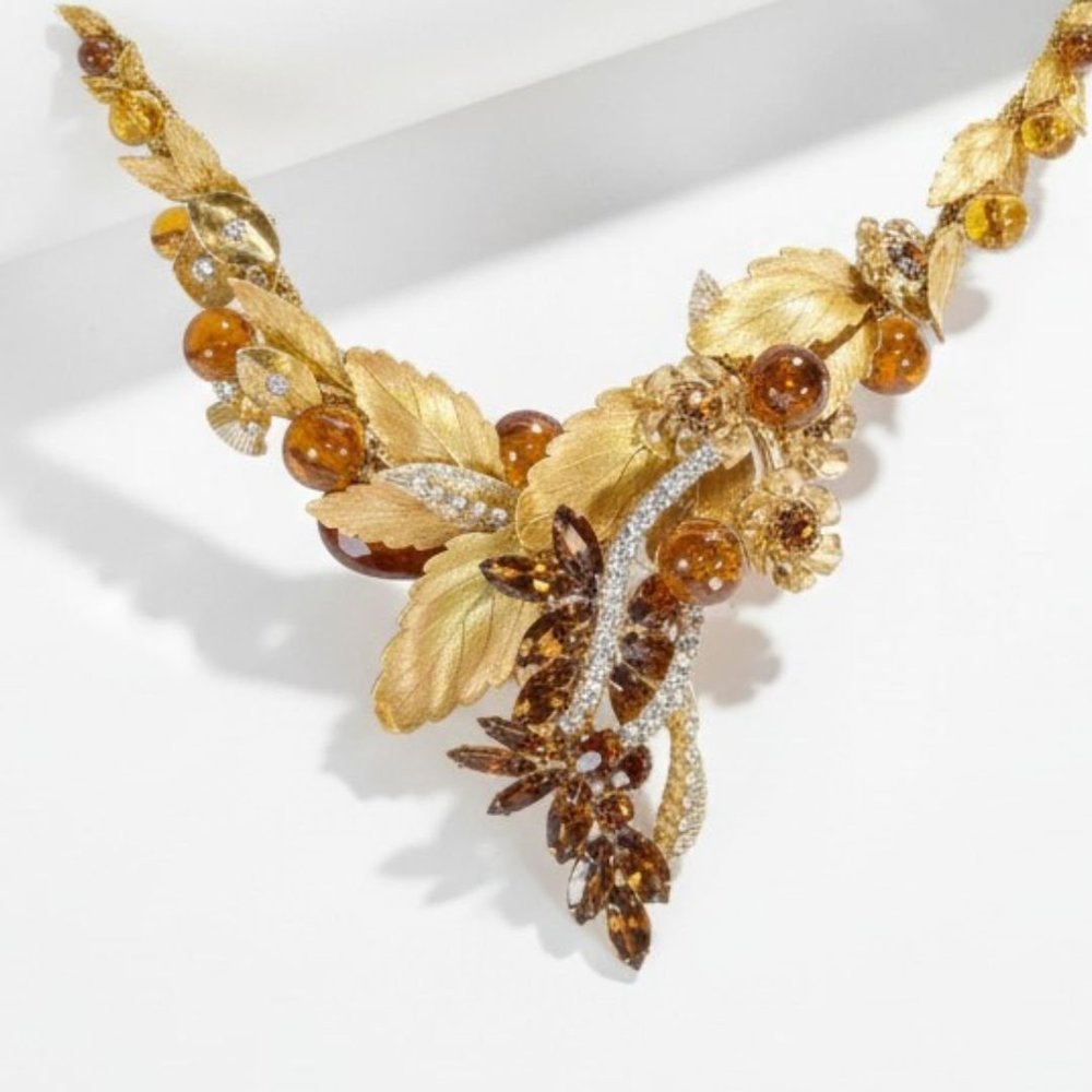 Close-up of an ornate gold leaf necklace with amber gemstones and sparkling floral details on a white background.