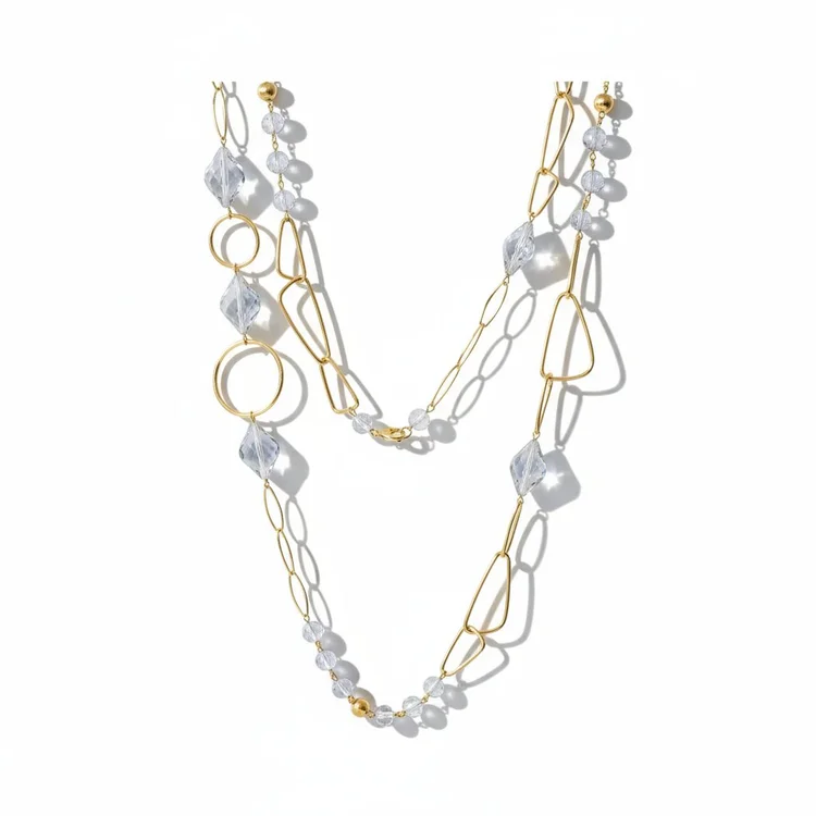 Long asymmetrical gold necklace with oversized link elements, circular accents, and clear faceted beads, photographed on a white background with sharp shadows.
