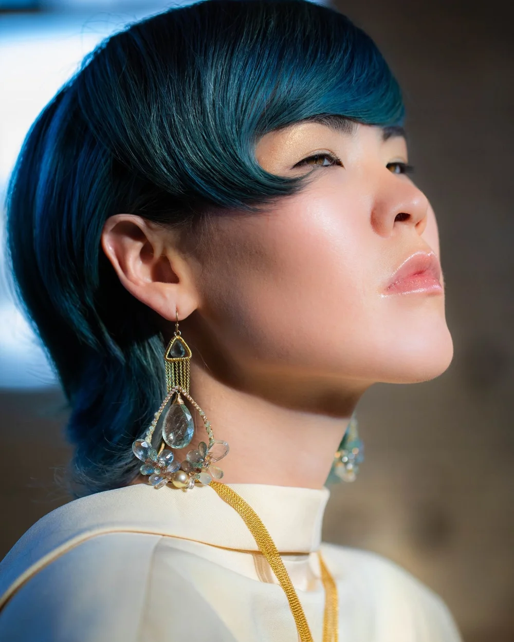 A model with teal hair and a white high collar wearing Andrea Li gold geometric gemstone earrings, by Andrea Li