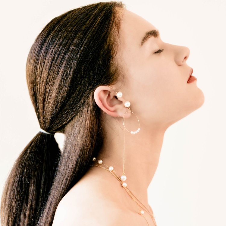 A model in profile with a low ponytail, wearing an Andrea Li pearl ear climber and gold hoop, by Andrea Li