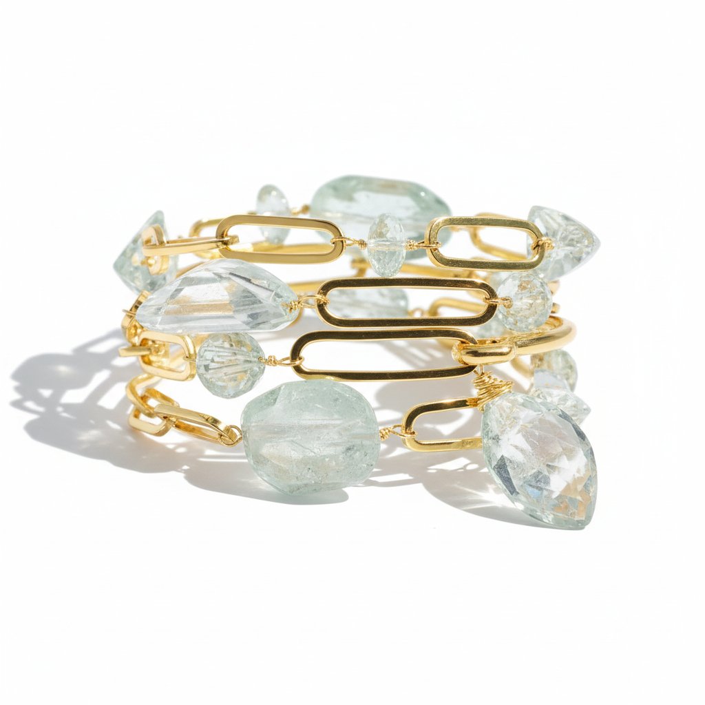 Gold link bracelet with oversized oval chain links and pale green translucent gemstones, photographed on a clean white background with soft shadows.