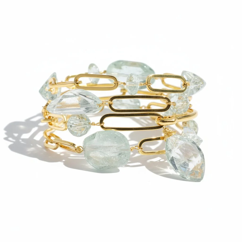 Gold link bracelet with oversized oval chain links and pale green translucent gemstones, photographed on a clean white background with soft shadows.