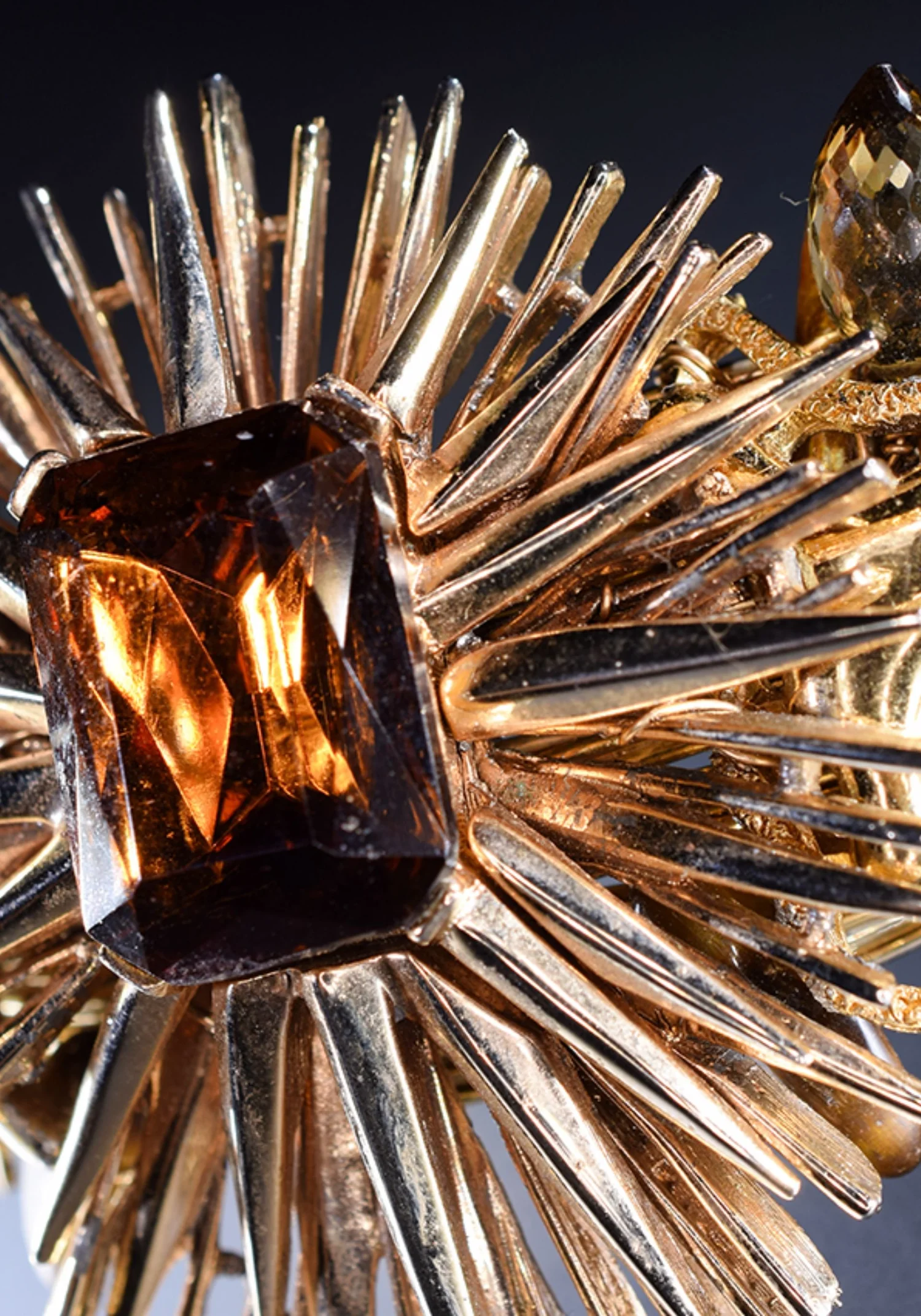 Close-up of a vintage gold starburst brooch with polished rays around a large emerald-cut amber-colored stone and a faceted drop