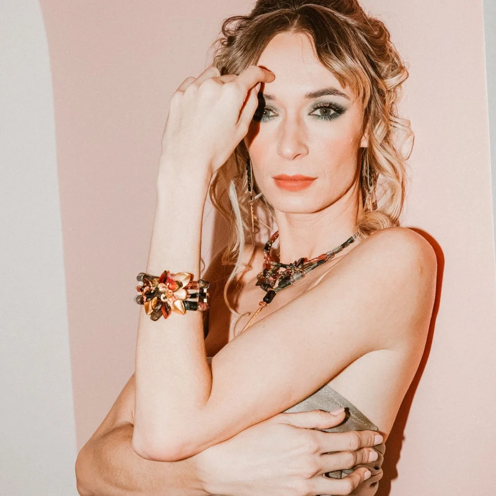 A model against a blush wall wearing a wide Andrea Li gemstone cuff on her raised arm