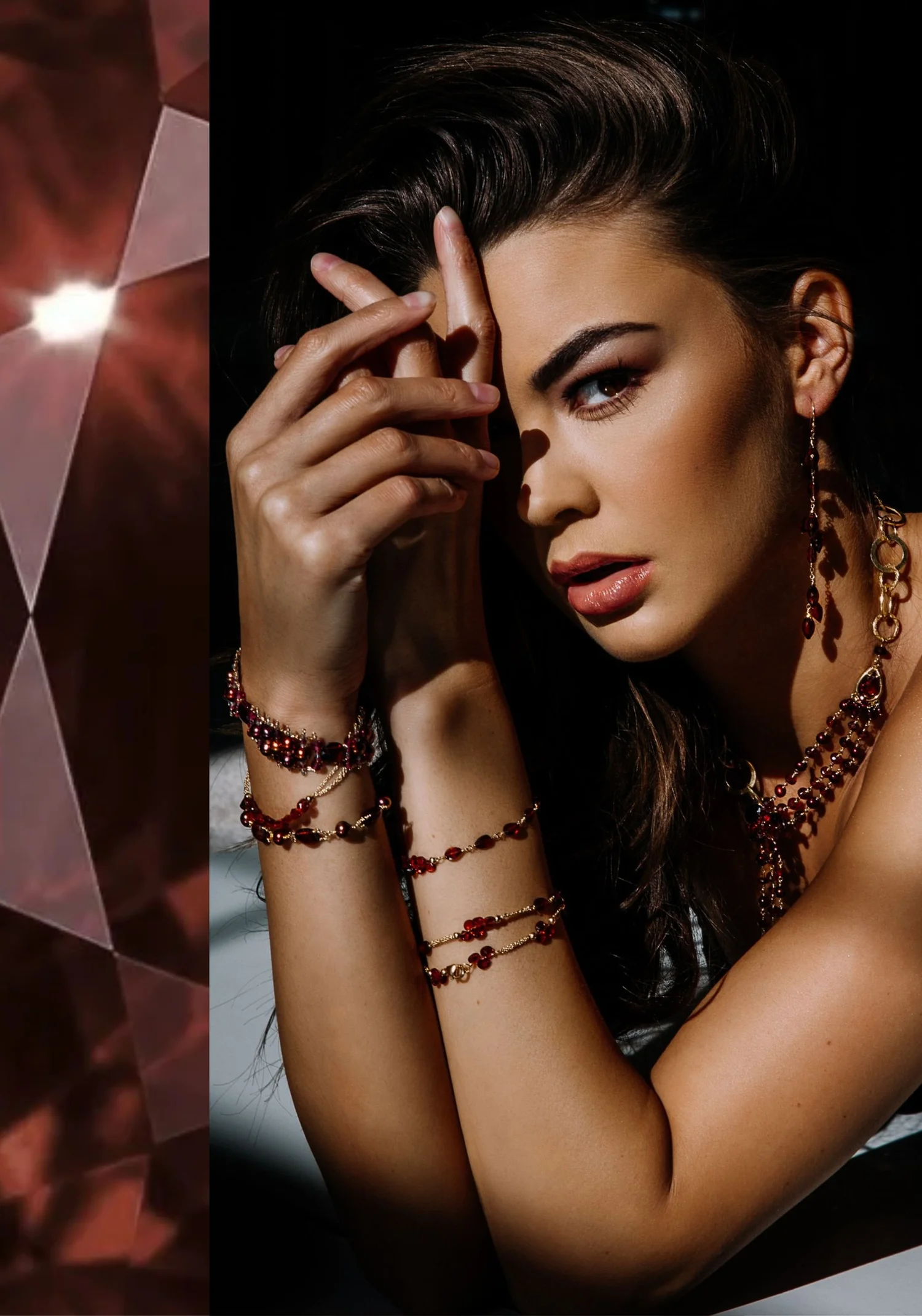 A model wearing layered gold bracelets, long drop earrings and a multi-strand necklace, all set with red garnet beads