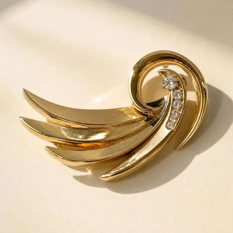 Mid-century-style gold swirl brooch with sweeping polished wings and a few clear stones