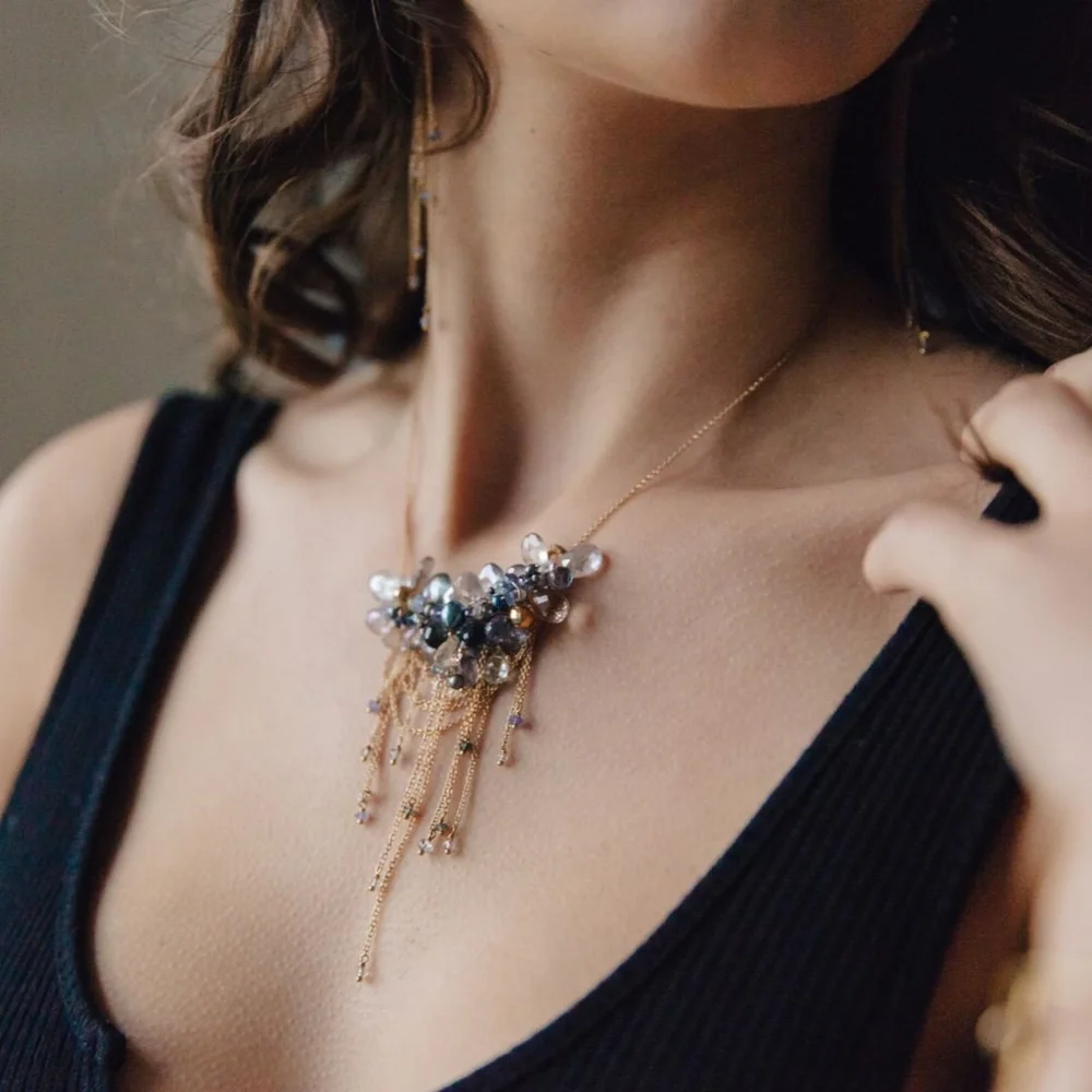 A model in a black V-neck wearing an Andrea Li gemstone cluster pendant with gold tassel drops