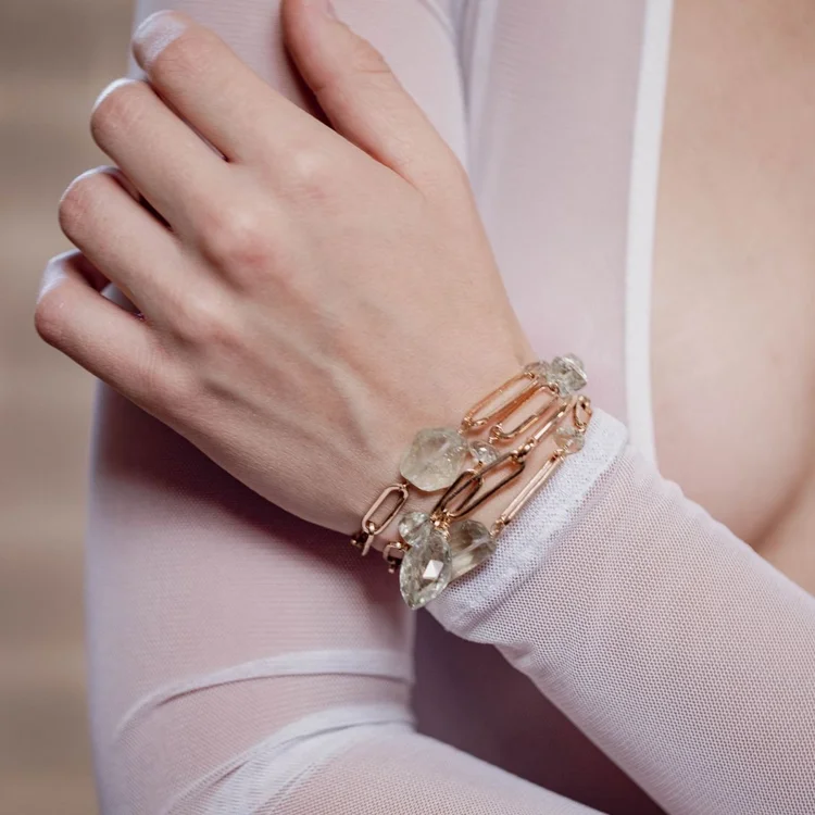A hand resting at the shoulder wearing a gold chain bracelet with clear stones