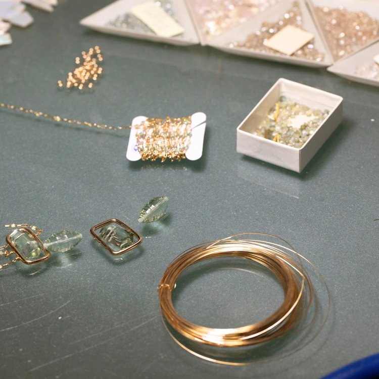 Coils of gold wire, wire-wrapped chain, rectangular wire frames and pale green stones on the bench