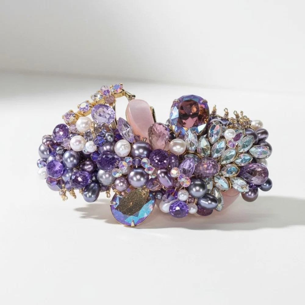 Close-up of a jeweled cuff bracelet with lavender crystals, pearls, and iridescent stones arranged in a dense floral cluster.